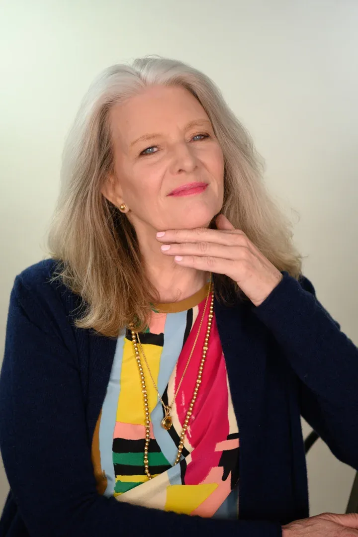 Patricia A. Tracy with a content smile, sitting with her hand on her hip, dressed in a vibrant blouse and dark sweater