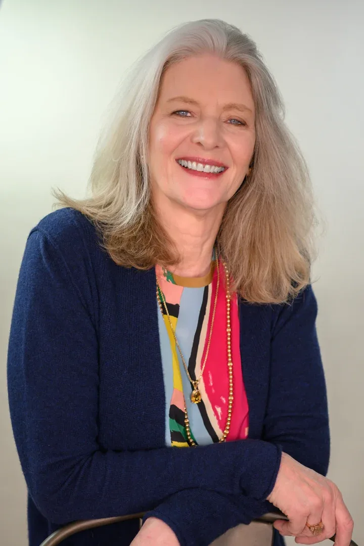 Patricia A. Tracy in a relaxed pose, smiling with her hand on her cheek, wearing a colorful blouse and navy cardigan