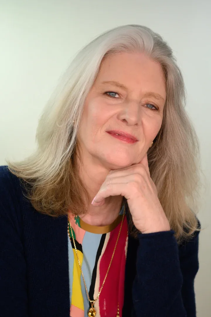 A cheerful Patricia A. Tracy looking directly at the camera, her hand resting on her chin, wearing a colorful blouse.