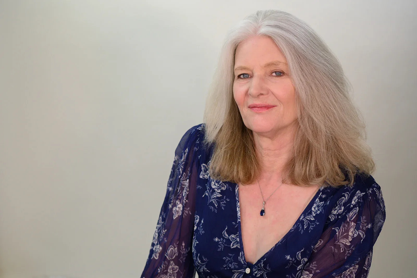 A close-up of Patricia A. Tracy, touching her face gently, smiling subtly, and adorned with elegant jewelry.