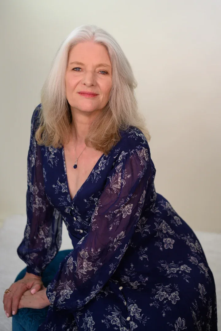 A portrait of Patricia A. Tracy, smiling warmly, dressed in a blue sweater over a bright, multicolored top.