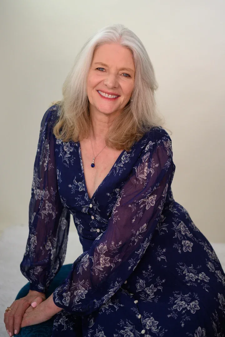 Patricia A. Tracy in a navy cardigan and vibrant blouse, smiling with a hand near her face, exuding a warm presence.